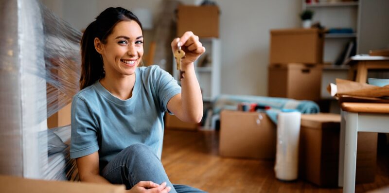 Young happy woman holds key while moving pa new home